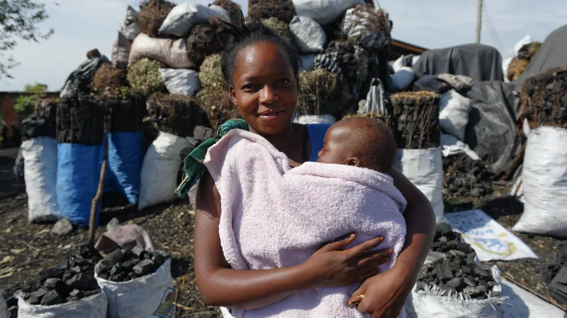 Woman smiling and holding baby in front of charcoal bags