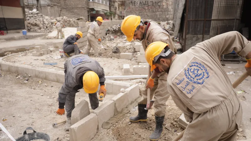 Three men work on rehabilitating sidewalk in Aleppo, Syria