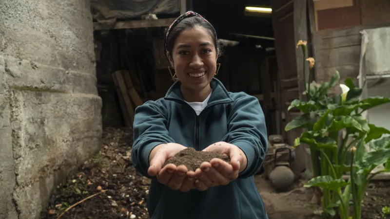 Smiling young woman facing the camera, holding soil in her hands