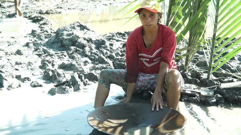 a female worker in a small-scale gold mine searching for gold and sitting on muddy water